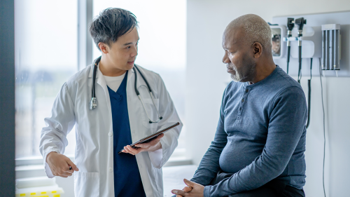 An Asian doctor and his patient, an older black man, discuss treatment in an exam room.