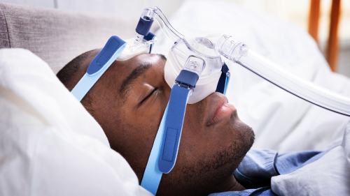 man sleeping with the aid of a Continuous Positive Airway Pressure (CPAP) machine mask strapped over his nose.