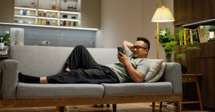 Man lying on a gray couch looking at his smartphone. 