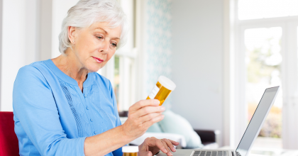 Older woman sitting in front of her laptop holding up a prescription drug bottle